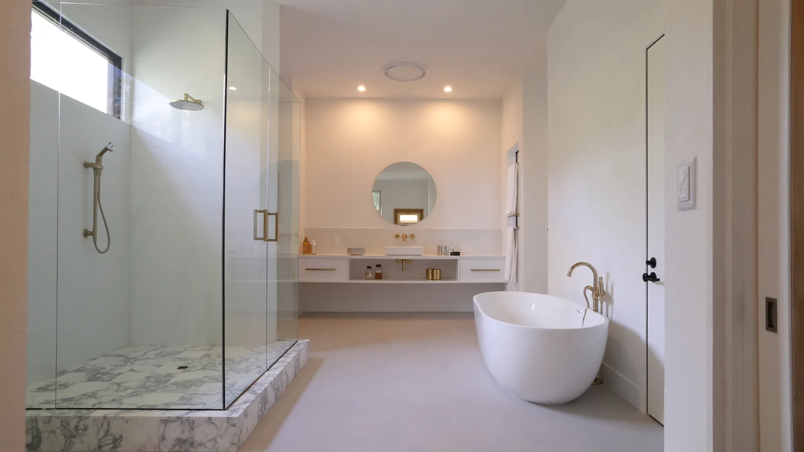 The same bathroom after remodel — curbless walk-in shower, large-format tile, floating double vanity, and warm gold fixtures